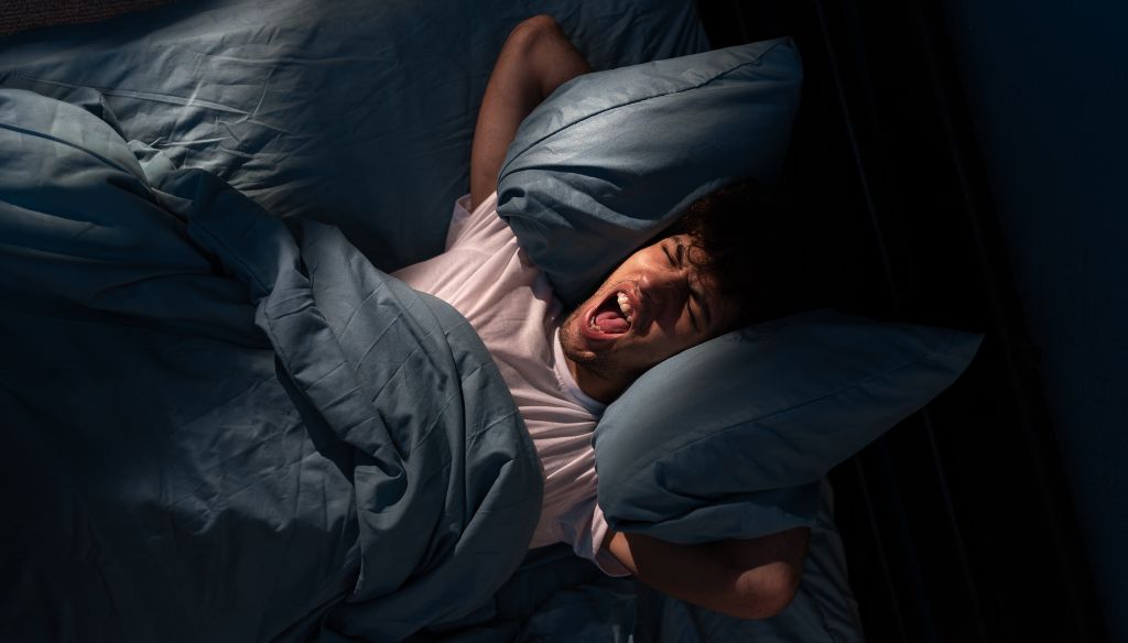 Annoyed man suffering neighbour noise in the bedroom at night at home.